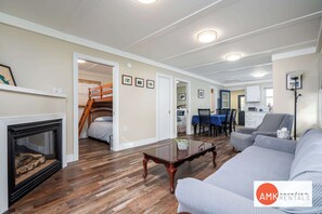 A spacious living room with hardwood flooring, a fireplace, a sofa, a dining area, and a staircase leading to another level.