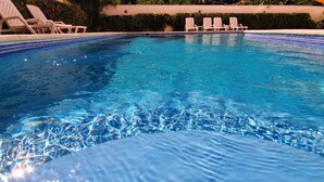 En swimmingpool med kristallklart blått vatten, omgiven av solstolar och en kant av kakel.