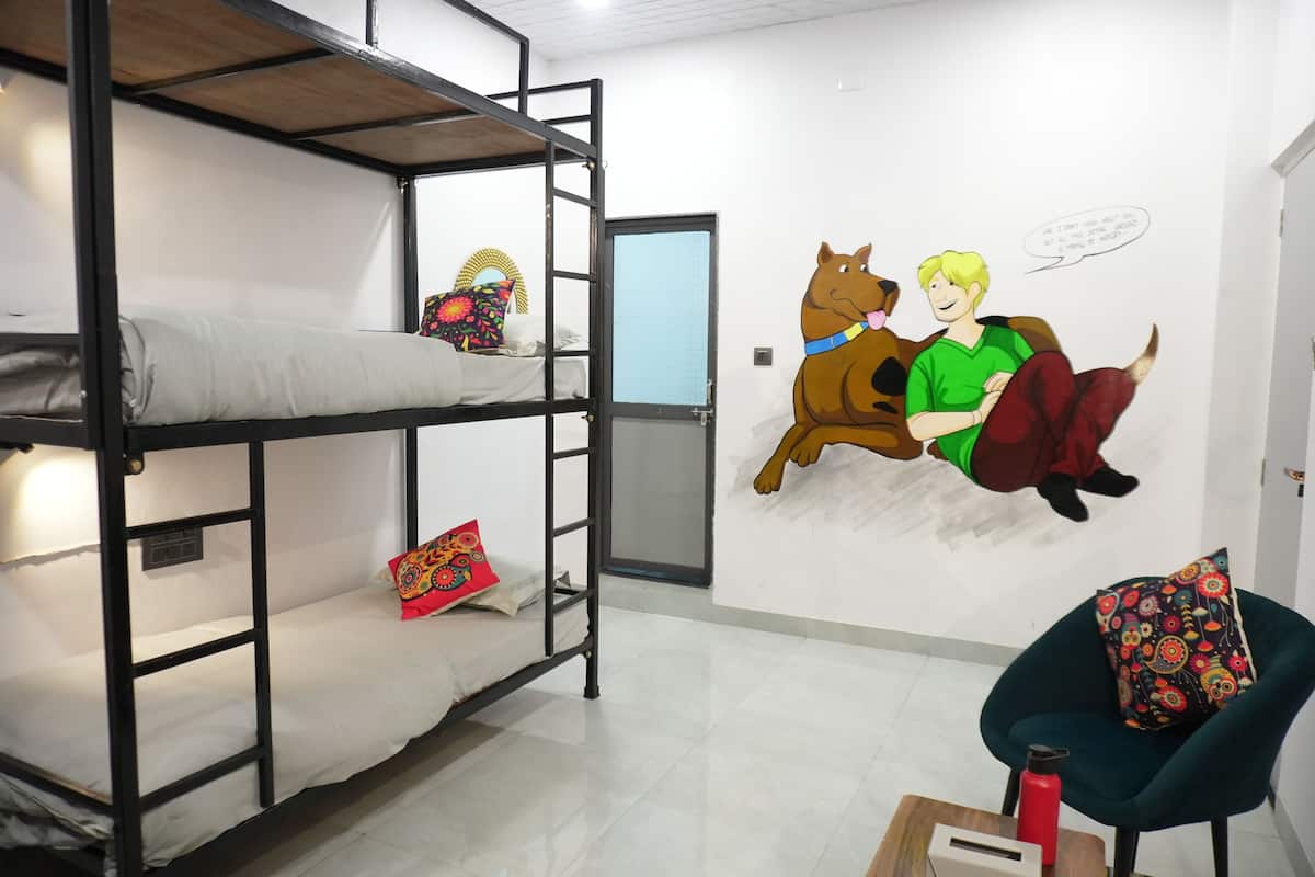 Une chambre avec un lit superposé orné d’une fresque représentant un personnage de dessin animé et un chien, ainsi qu’une chaise et une bouteille d’eau rouge posée sur une table.