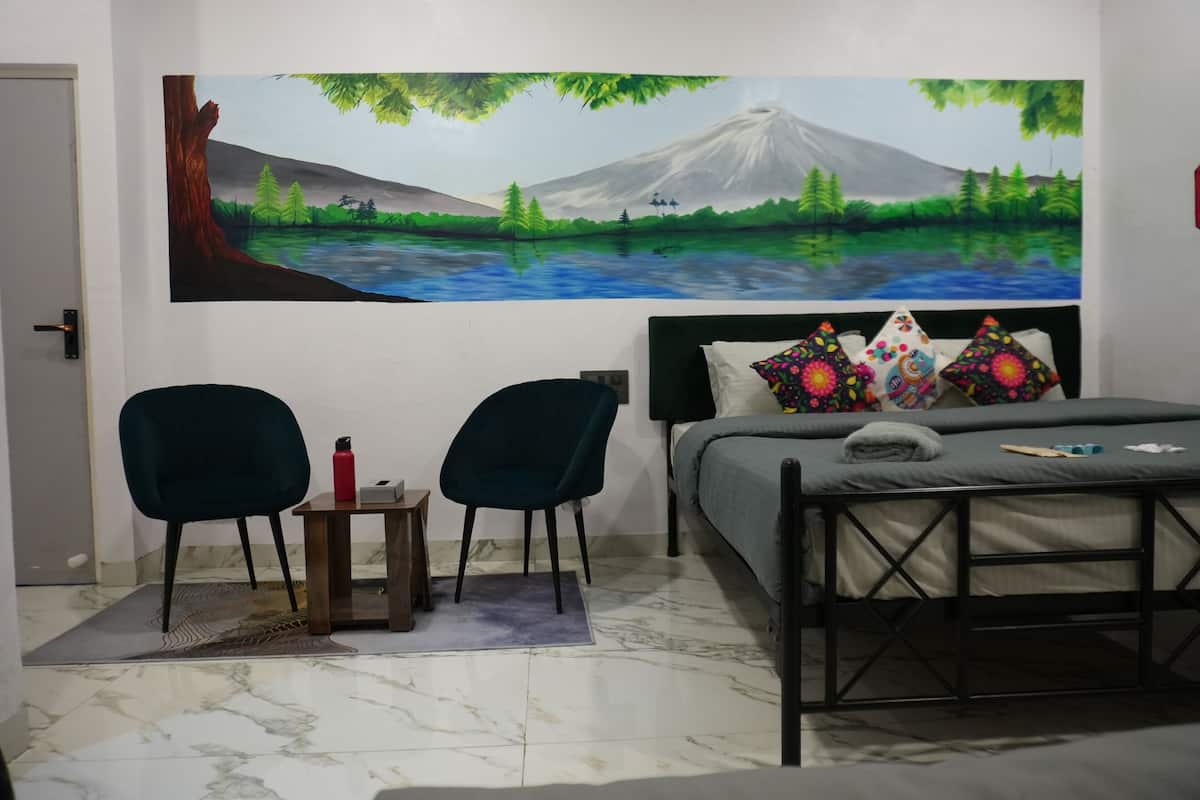 Une chambre à coucher avec un lit, deux chaises, une petite table et un tableau représentant un paysage accroché au mur.