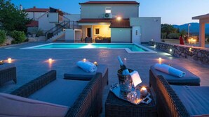 A modern villa with a swimming pool, outdoor seating, and a well-lit entrance.