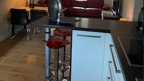 A modern kitchen with a central island, a dining area with a red sofa, and a living area with a red couch.