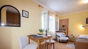 A cozy room with a wooden dining table, two white chairs, a sofa, and a bed.