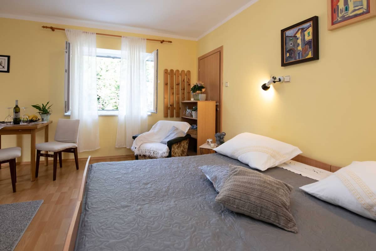 A bedroom with a large bed, a chair, a desk, and a window with curtains.