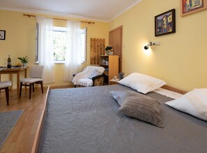 A bedroom with a large bed, a chair, a desk, and a window with curtains.