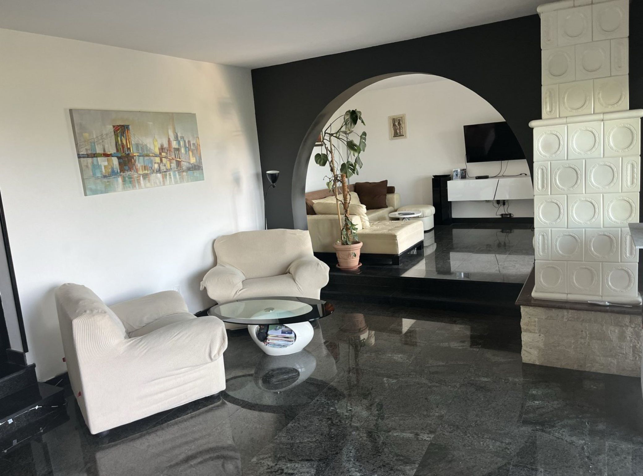 A modern living room with a sofa, armchair, and coffee table, a painting on the wall, and a TV in the background.