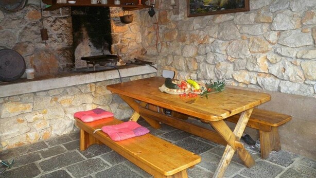 A rustic stone interior with a wooden table and benches, a stone fireplace, and a painting on the wall. - Serene Garden Apartment With Terrace (Moscenicka Draga)