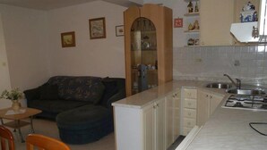 A compact living space with a kitchenette, a sofa, a dining table, and a small kitchen counter. - Serene Garden Apartment With Terrace (Moscenicka Draga)