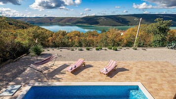 A swimming pool with lounge chairs and a view of a lake and mountains.