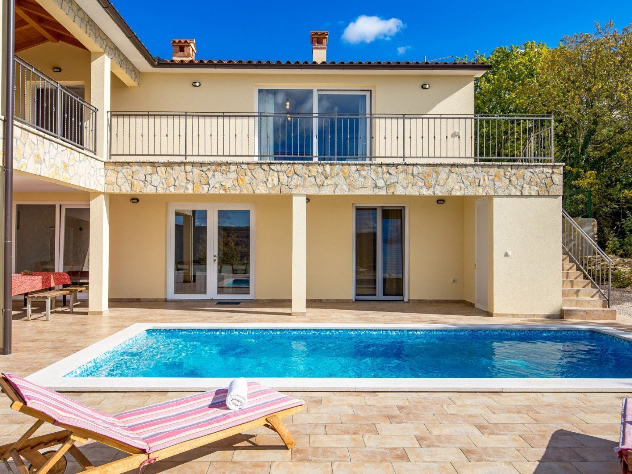 A two-story house with a swimming pool, a balcony, and a stone facade.