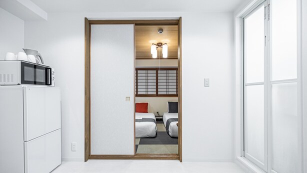 Een hotelkamer met een schuifdeur naar een slaapkamer met twee bedden, een magnetron en een koelkast.