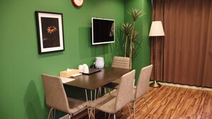 Een vergaderruimte met een groene wand, een klok, een lijst, een flatscreen-tv, een koffiezetapparaat en een potplant.