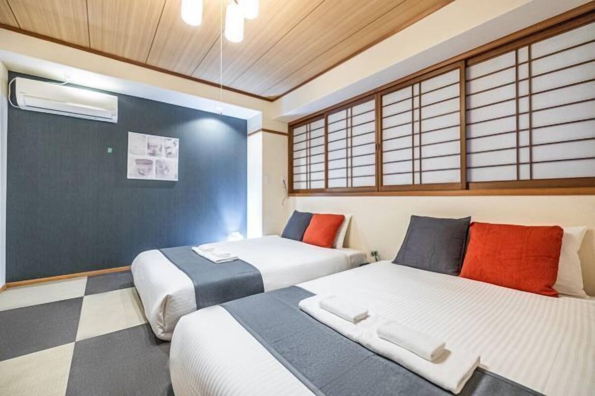 A hotel room with two beds, a checkered floor, an air conditioning unit, and a shoji screen.