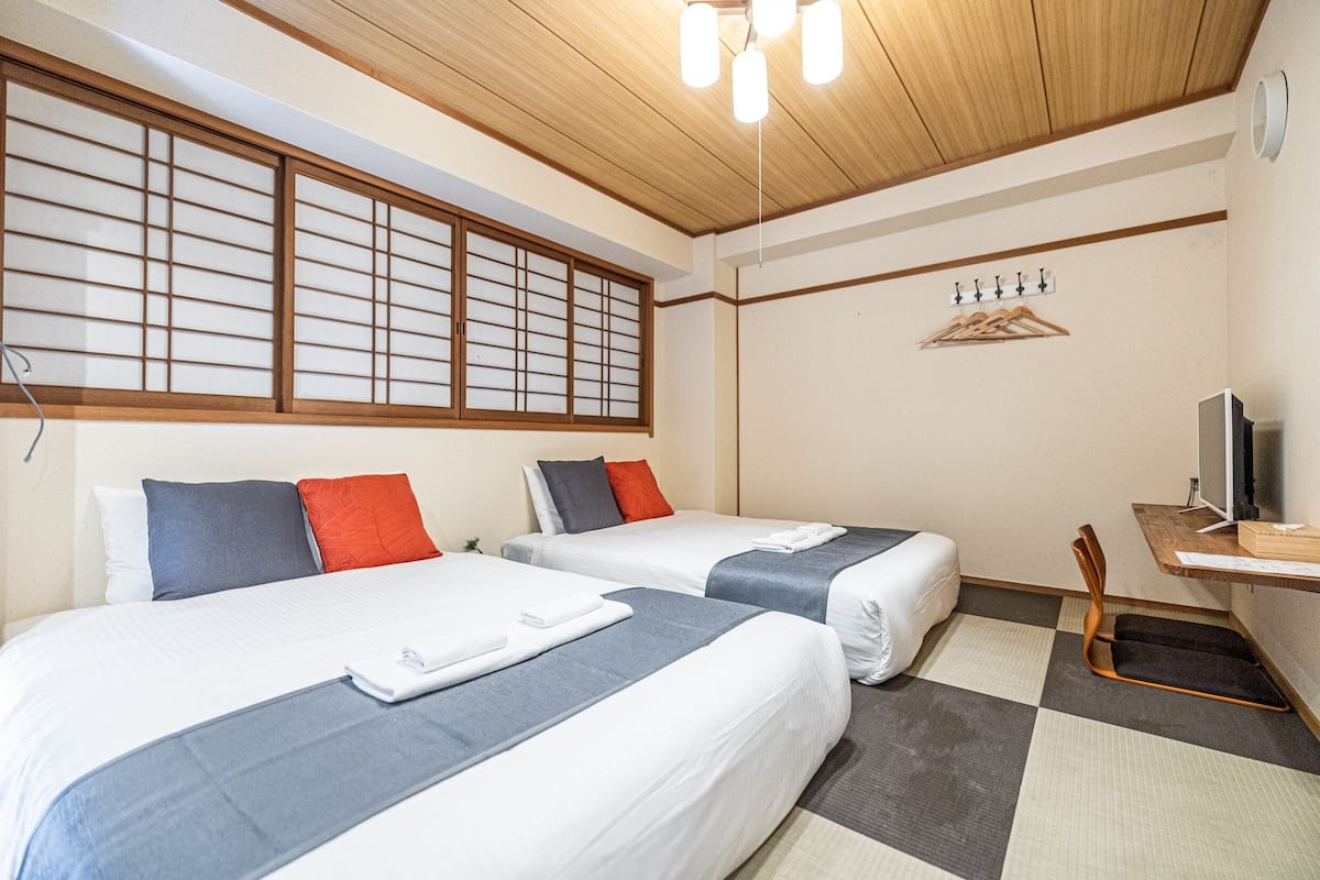 A hotel room with two beds, a television, a wooden ceiling, and a window with a view.