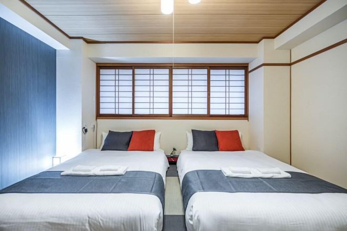 A hotel room with two beds, a large window with shoji screens, and a wooden ceiling.