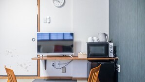 Een compacte kamer met een flatscreen-tv, een magnetron en een kleine koelkast. Er zijn twee houten stoelen en een bijzettafeltje.
