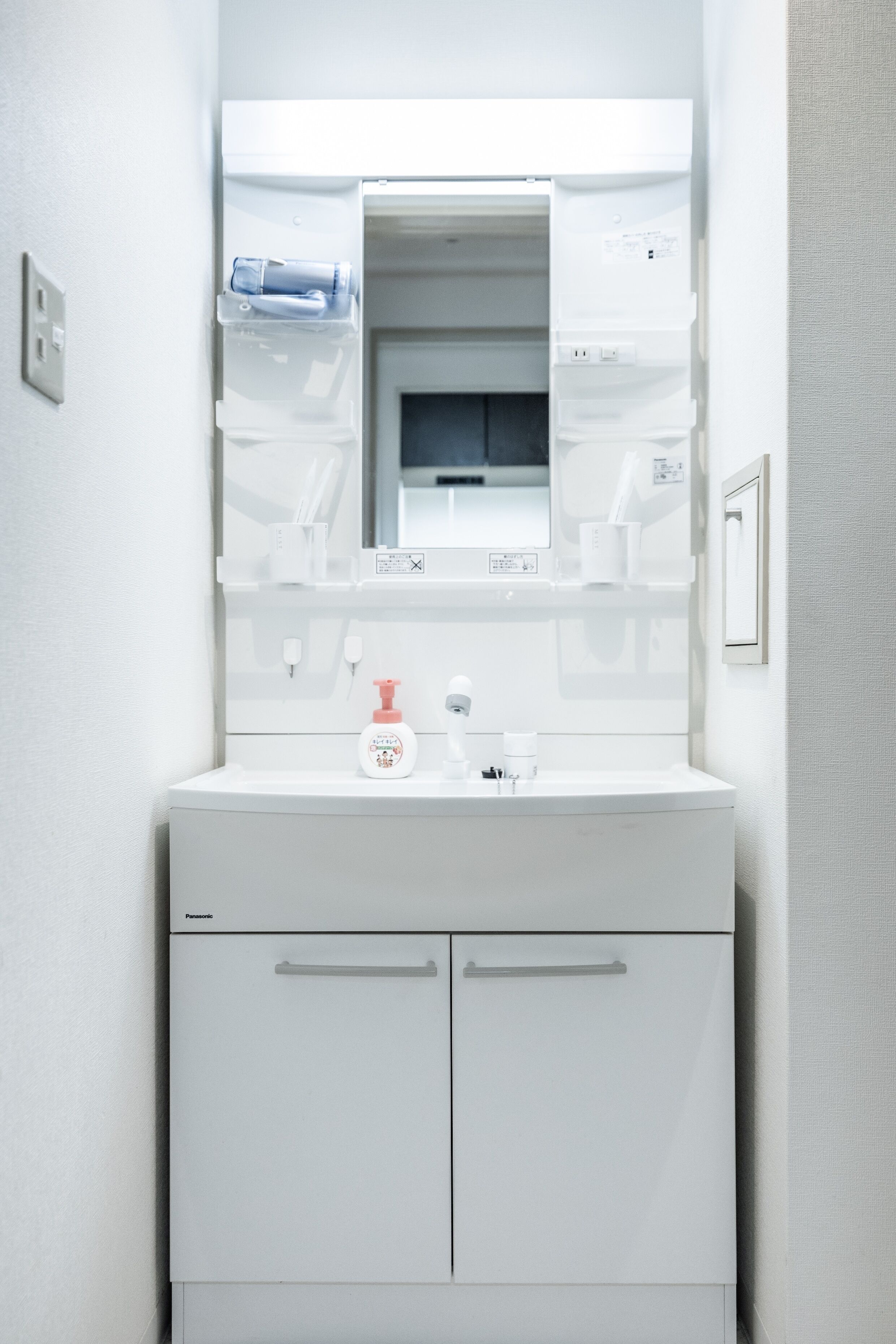 A white bathroom vanity with a mirror, a towel dispenser, and a soap dispenser.