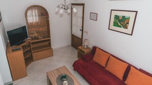 A compact living space with a TV, a red sofa, a wooden coffee table, a glass cabinet with wine glasses, and a ceiling fan. - Charming Apartment With Sea Views and Shared Pool (Lovran)