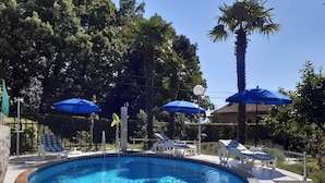 A swimming pool with lounge chairs and umbrellas, surrounded by trees and a clear sky. - Charming Apartment With Sea Views and Shared Pool (Lovran)