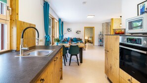 A modern kitchen with a sink, wooden cabinets, a dining area with a table and chairs, and a living room with a sofa. - Apartment 'Untere Ferienwohnung' with Private Terrace, Shared Garden and Wi-Fi (Meßstetten)