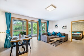A living room with a sofa, coffee table, dining table, and chairs. There are large windows with curtains, a light fixture, and a brick wall. - Apartment 'Untere Ferienwohnung' with Private Terrace, Shared Garden and Wi-Fi (Meßstetten)