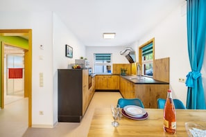 A compact kitchen with wooden cabinets, a dining table with chairs, and a window with blinds. - Apartment 'Untere Ferienwohnung' with Private Terrace, Shared Garden and Wi-Fi (Meßstetten)