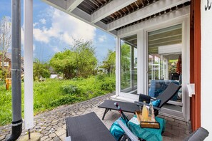 Un'area relax all'aperto con sedie a sdraio, un tavolo con una bevanda e vista su piante e un edificio.