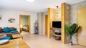 A modern living room with a flat-screen TV, a dining table set, a sofa, and a large plant. - Apartment 'Untere Ferienwohnung' with Private Terrace, Shared Garden and Wi-Fi (Meßstetten)