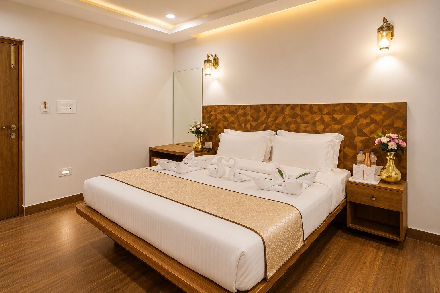 A hotel room with a large bed, wooden headboard, bedside tables, a mirror, and wall-mounted lights.