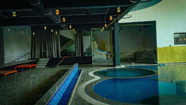 Piscina interior com borda azulejada, escadaria que leva a uma varanda e área de estar com bancos vermelhos.