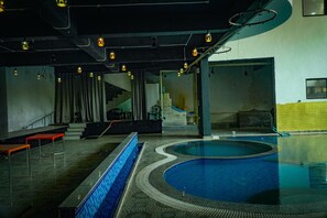 Ein Innenpool mit Fliesenrand, eine Treppe zu einem Balkon und eine Sitzgruppe mit roten Bänken.