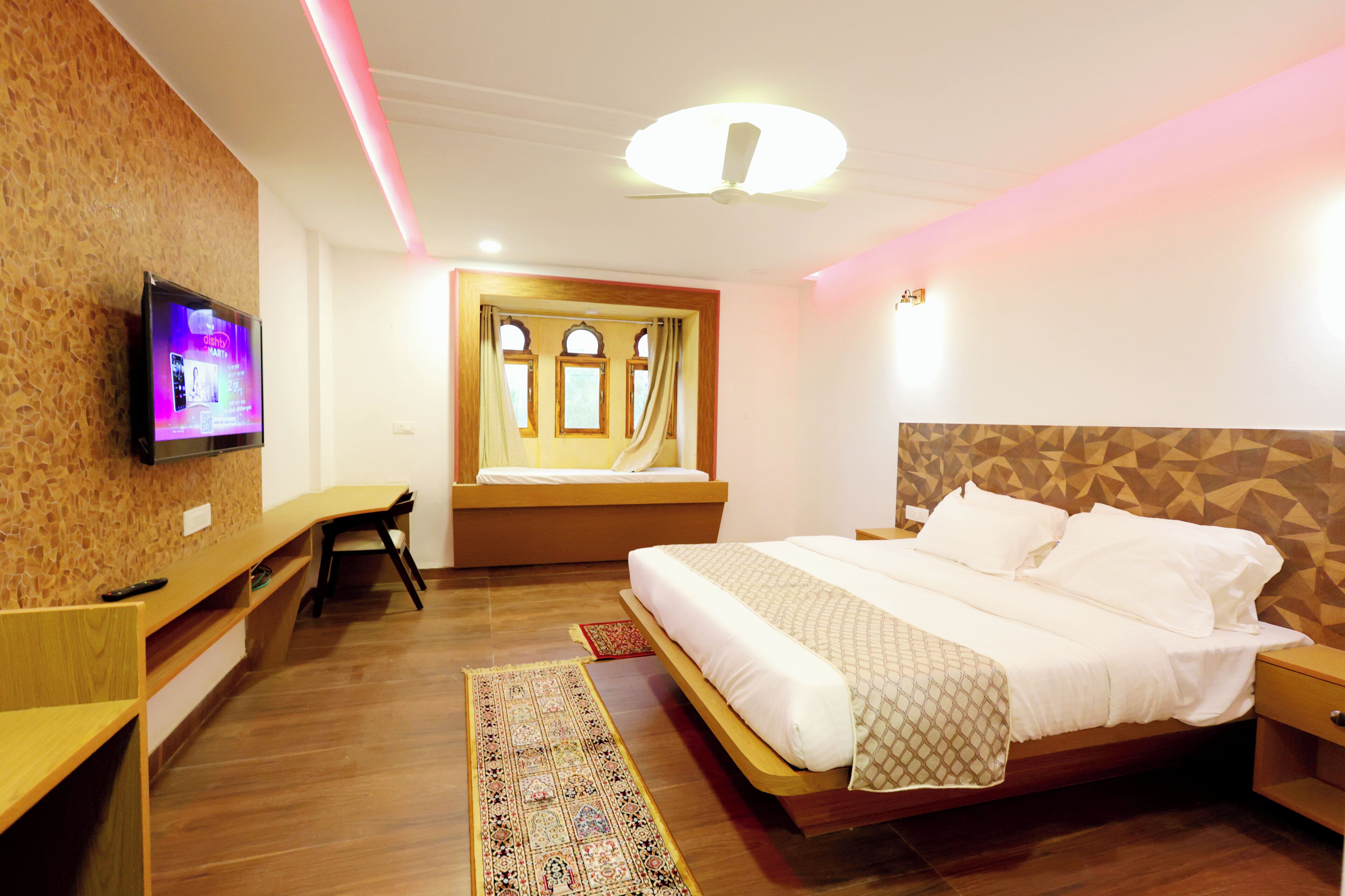 Ein modernes Hotelzimmer mit einem hölzernen Bett, einem Schreibtisch, einem Fernseher und einem gemusterten Teppich.