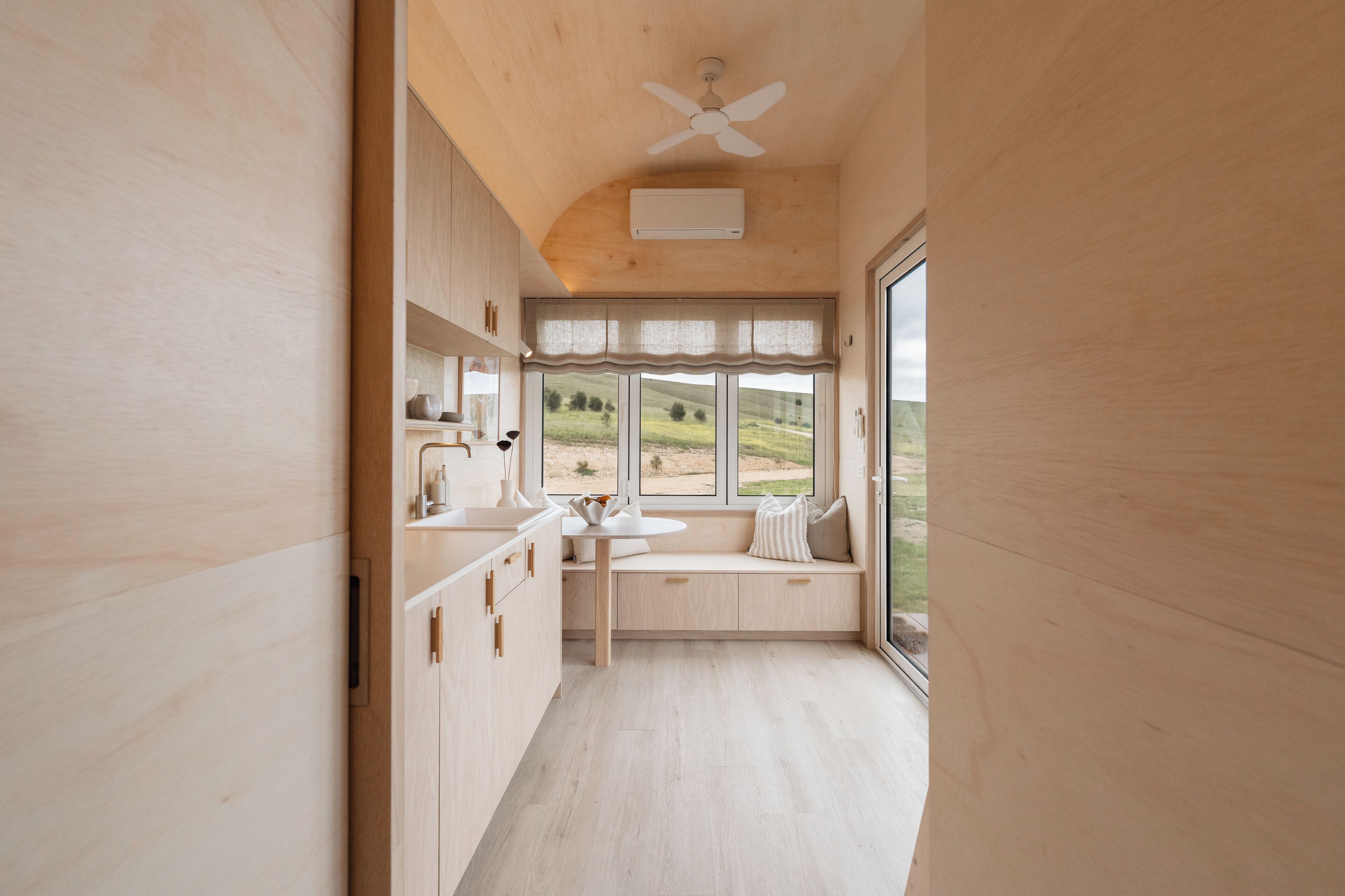 Eine moderne Küche mit Holzschränken, einer integrierten Sitzbank und einem großen Fenster mit Blick ins Freie.