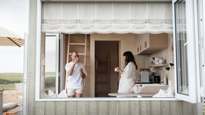 A compact, open-plan living space with a kitchenette, a dining area, and a large window overlooking a natural landscape.