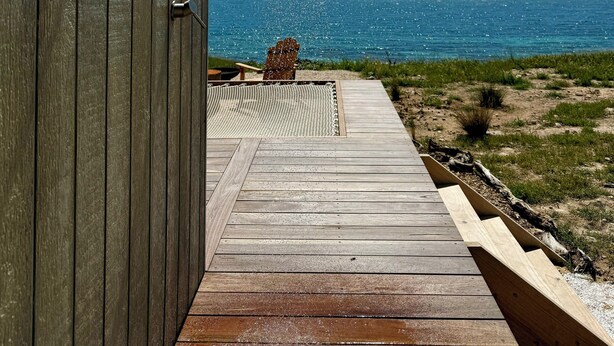 A wooden door with a showerhead, a wooden deck leading to a beach view.