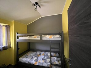 Habitación con literas, ventilador de techo, una puerta y una ventana con cortinas.