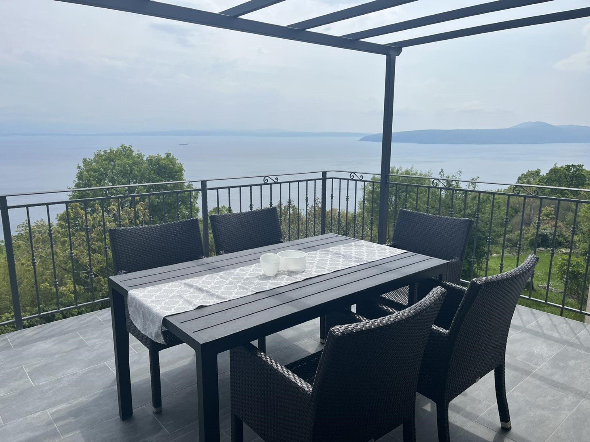 Terraço com mesa e cadeiras, com vista para um corpo de água e vegetação.