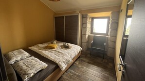 A bedroom with a bed, two pillows, a chair, a window, and a stone wall. - Splendid Holiday Home With Panoramic Sea Views Moscenicka Draga (Moscenicka Draga)