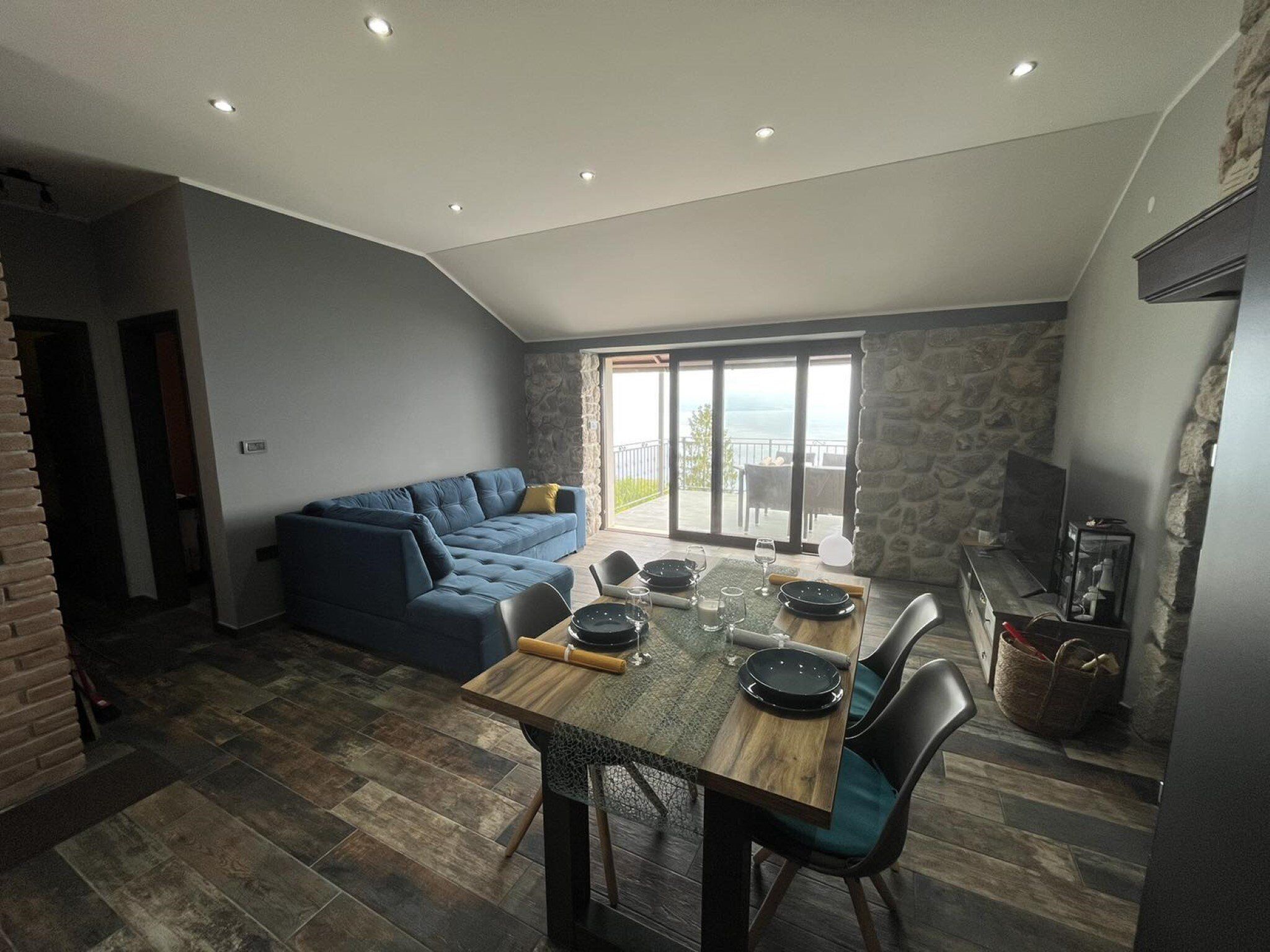 A dining area with a wooden table set for four, a blue sofa, and a stone wall.