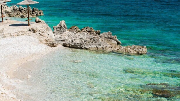 A beach with clear turquoise water, rocky formations, and a few umbrellas. - Stylish Two Bedroom Apartment in Labin (Labin)
