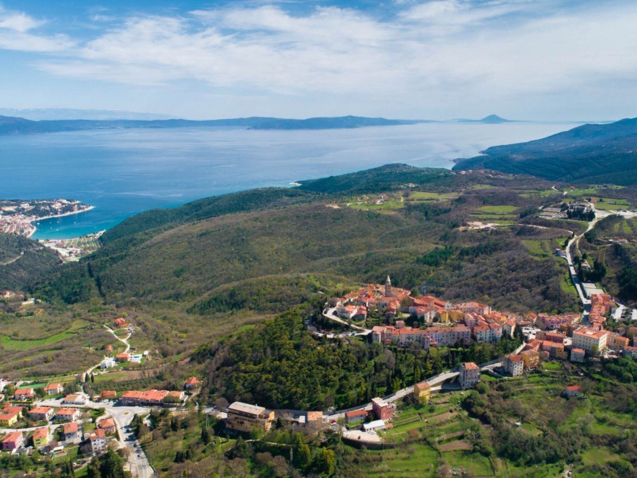 An aerial view of a coastal town with a central cluster of buildings, roads, and surrounding greenery.