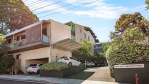 Un immeuble résidentiel doté d’un espace de stationnement couvert, d’un balcon et d’une enseigne indiquant « 16-20, rue East Crescent ».