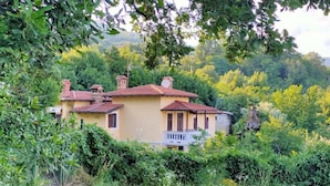 A yellow villa with a red-tiled roof, surrounded by lush greenery and trees.