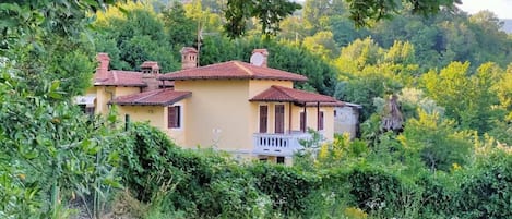 A yellow villa with a red-tiled roof, surrounded by lush greenery and trees.