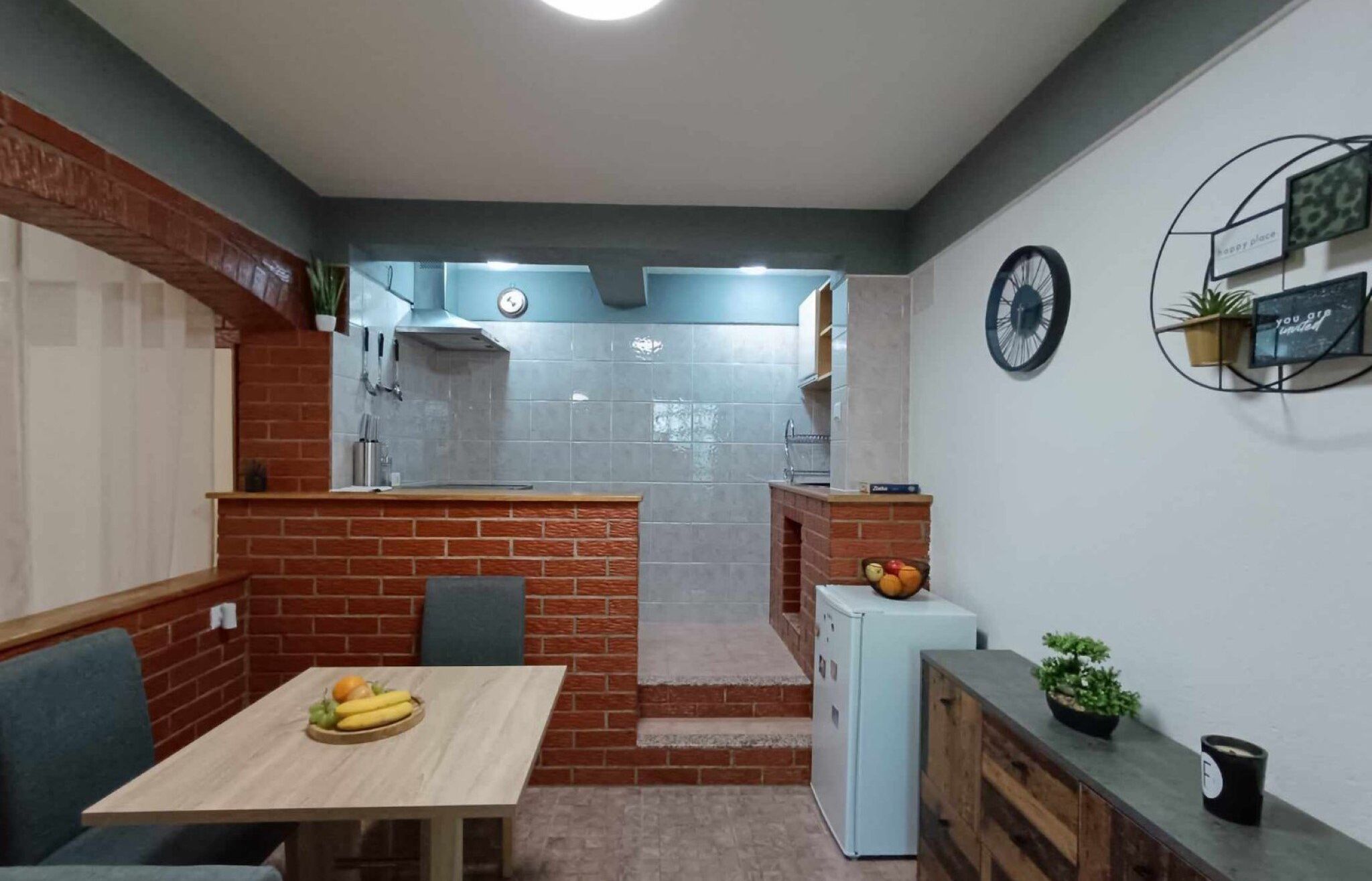 A compact kitchen with a brick accent wall, a small refrigerator, and a dining area with a table set for two.