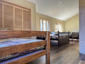A wooden bench with a patterned cushion in a room with wooden floors, a high ceiling, and a view of a bed in the background. - Heated Indoor Private Pool | Stream Front | Game Room (Cresco)
