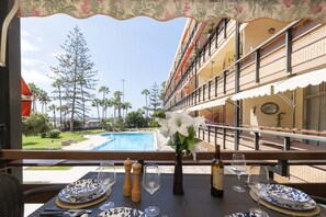 Un coin repas avec une table dressée pour deux personnes, donnant sur une piscine et un jardin aménagé.
