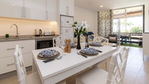 A modern kitchen with white cabinetry, a dining table set for four, and a view of the outdoors through large windows. - Sea Breeze Frontline Apartment (Los Cristianos)