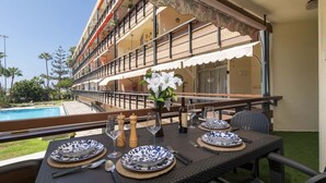 A dining table set with plates, cutlery, and a bottle, overlooking a pool and a building with balconies. - Sea Breeze Frontline Apartment (Los Cristianos)