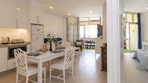 A modern kitchen with white cabinets, a dining area with a white table and chairs, and a view of the outdoor patio. - Sea Breeze Frontline Apartment (Los Cristianos)